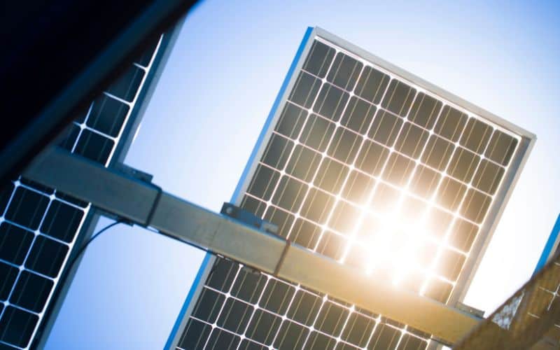 Solar panel mounted on a metal frame against a clear sky, with sunlight flaring through the panel.
