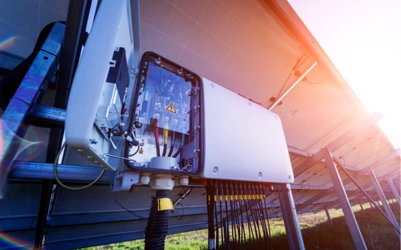 Inverter box attached to solar panels, with sunlight flaring in the background.