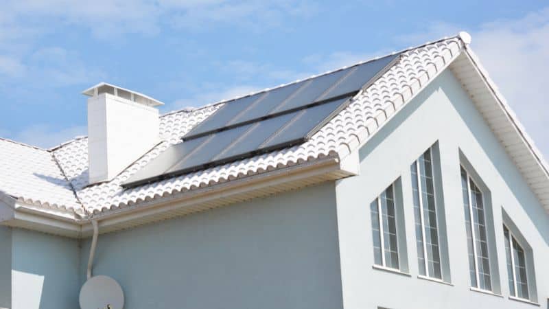 White house with a tiled roof, solar panels, and chimney beneath a blue sky with scattered clouds.