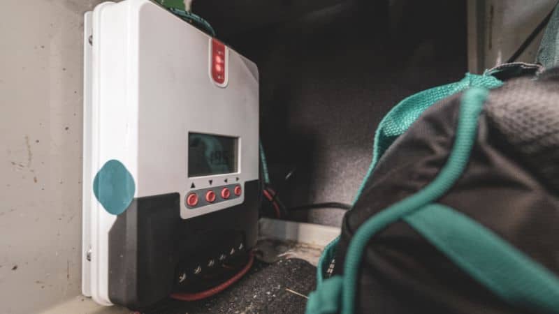 Electronic device with screen and red buttons on a wall, partly blocked by a green and black bag in front.