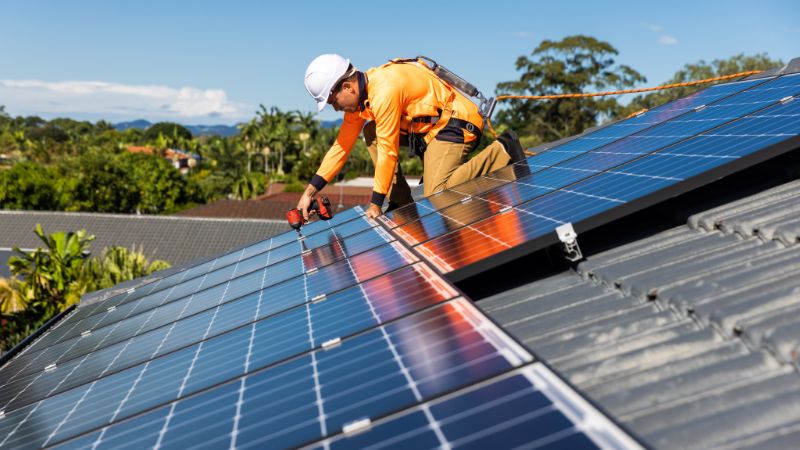 Solar panel installation technician on rooftop solar energy system in progress.